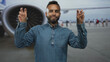 © Krakenimages.com - Man in denim shirt showing peace sign with both hands near airplane engine on airport tarmac; joyful travel fun.