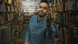 © Krakenimages.com - Man shows middle finger toward camera in a library building aisle lined with books and shelves; defiance protest.