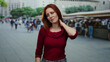 © Krakenimages.com - Woman touching neck in outdoor market street with redhead hair wearing red sweater appears in pain amidst busy urban scene with blurred background pedestrians