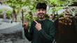 © Krakenimages.com - Young man smiling enthusiastically in a park setting, with lush green foliage, pointing upwards during a bright sunny day.