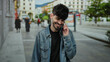 © Krakenimages.com - Young man smiling on phone in urban street wearing denim jacket amidst city background environment.