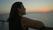 © Krakenimages.com - Woman leans on cruise ship rail, looking toward the horizon, showing a bare shoulder and resting hand to neck on deck at sunset; serenity.
