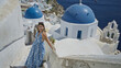 © Krakenimages.com - Woman touching railing while walking down white steps beside blue church dome on building in santorini; serenity travel escape.