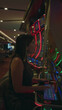 © Krakenimages.com - Woman presses a slot machine button with hand on button, smiling while seated by neon slot machines in casino; joyful anticipation.