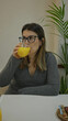© Krakenimages.com - Woman sipping orange juice at a luxury modern restaurant, seated indoors, wearing glasses and a gray sweater near a potted plant, exemplifying a relaxed and elegant atmosphere.
