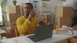 © Krakenimages.com - Young black man holding a smartphone and pointing at the screen in a studio filled with cardboard boxes and a laptop on a desk; concentration.