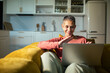 © Marko Geber - Senior woman video chatting on laptop on sofa in home kitchen