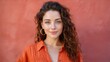 © buraratn - Beautiful young woman with curly hair and blue eyes smiling warmly against a vibrant red wall, showcasing natural beauty and confidence in casual attire
