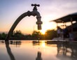 © Fan - A water faucet with a single drop falling at sunset