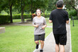 © Shutter2U - A jogger with headphones and a walker pass each other on a park pathway surrounded by lush greenery.