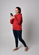 © faestock - full length figure of female model wearing  basic contemporary casual clothing, red hoodie jumper, skinny jeans, sneakers. standing walking pose holding cell phone mobile,  isolated white studio backg