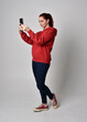 © faestock - full length figure of female model wearing  basic contemporary casual clothing, red hoodie jumper, skinny jeans, sneakers. standing walking pose holding cell phone mobile,  isolated white studio backg