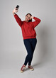 © faestock - full length figure of female model wearing  basic contemporary casual clothing, red hoodie jumper, skinny jeans, sneakers. standing walking pose holding cell phone mobile,  isolated white studio backg