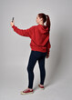 © faestock - full length figure of female model wearing  basic contemporary casual clothing, red hoodie jumper, skinny jeans, sneakers. standing walking pose holding cell phone mobile,  isolated white studio backg