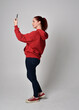 © faestock - full length figure of female model wearing  basic contemporary casual clothing, red hoodie jumper, skinny jeans, sneakers. standing walking pose holding cell phone mobile,  isolated white studio backg