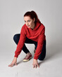 © faestock - full length figure of female model wearing  basic contemporary casual clothing, red hoodie jumper, skinny jeans, sneakers.  kneeling on floor  isolated white studio background.