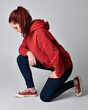 © faestock - full length figure of female model wearing  basic contemporary casual clothing, red hoodie jumper, skinny jeans, sneakers.  kneeling on floor  isolated white studio background.