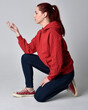 © faestock - full length figure of female model wearing  basic contemporary casual clothing, red hoodie jumper, skinny jeans, sneakers.  kneeling on floor  isolated white studio background.