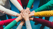 © Meniya - Image is a vibrant, top-down photograph featuring a diverse group of people placing their hands together in the center, symbolizing unity and teamwork. The hands vary in skin tones, showcasing friend