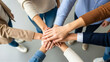 © vladnikon - Top down view of a diverse group of people standing in a circle putting their hands together in the center showing unity and teamwork