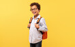 © Prostock-studio - Happy black schoolboy with curly hair, wearing glasses and smiling at camera, carrying an orange backpack on sunny yellow background