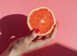 © ink drop - Close-up of a woman’s hand holding a juicy pink grapefruit with soft pink tones