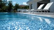 © cha - Crystal clear blue swimming pool water with sparkling reflections, a modern luxury villa, and sun loungers on a bright, sunny day.
