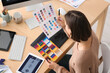 © Pixel-Shot - Young female graphic designer working with color samples at table in office