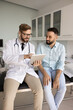 © fizkes - Patient education and guidance. Attentive smiling doctor share expertise with male visitor on consultation in clinic use digital pad for easy visualization medical information about disease diagnosis