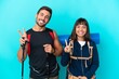 © luismolinero - Young mountaineer couple with a big backpack isolated on blue background smiling and showing victory sign