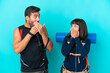 © luismolinero - Young mountaineer couple with a big backpack isolated on blue background covering mouth with hands for saying something inappropriate