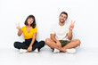 © luismolinero - Young couple sitting on the floor isolated on white background smiling and showing victory sign