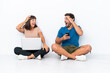 © luismolinero - Young couple sitting on the floor holding pc and mobile phone isolated on white background with surprise and shocked facial expression