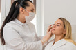 © Andrii Iemelianenko - Young woman sits in chair while cosmetologist in mask gently inspects facial skin before treatment. Adult client in white robe feels calm trusts professional skincare evaluation in modern clinic room.