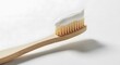 © RONY MIAH - Bamboo toothbrush with white toothpaste on bristles against a plain white background
