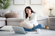 © wattana - Young woman sitting on the living room floor using a laptop at home. Concept of remote work, online learning, and home lifestyle.