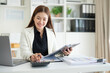 © wattana - Professional accountant using a calculator while reviewing financial reports at her desk.