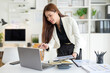 © wattana - Professional accountant reviewing financial reports and pointing at a laptop screen while standing at her desk.