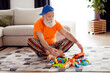 © deagreez - Playful grandpa in bright living room enjoys building blocks and toy truck indoors on a cozy weekend at home