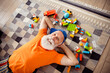 © deagreez - Funny elderly man relaxes on a patterned rug surrounded lego blocks enjoying playful home time indoors in a cozy casual setting