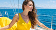 © NeuroCake - Young woman in yellow dress standing on yacht deck. Female enjoying sailing trip on blue ocean. Summer travel concept