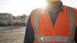 © Vyatcheslav - Construction worker wearing orange safety vest and hard hat on site. Unrecognizable male engineer standing outdoors with sun flare