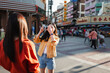 © Parichat - Young woman taking friend's picture on Bangkok street