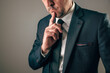 © Bits and Splits - Businessman in dark suit resting index finger thoughtfully on chin with serious gaze.