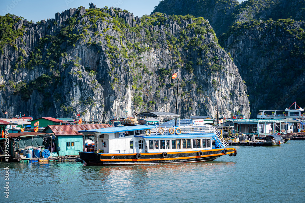 Touristenboot im schwimmenden Dorf vor Karstfelsen in Vietnam