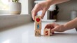 © VisiNode Studio - Hands stacking wooden blocks with icons of apple, water bottle, sneaker, and can on kitchen counter.