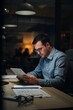 © olegganko - Man Reading on Tablet at Desk in Office During Evening Time