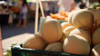 © Sergio IQstock - cantaloupe melons at a real street market, handheld candid feel but technically ultra sharp, melons stacked in a plastic crate on a vendor table, background shows shoppers and othe