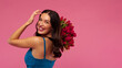 © Home-stock - Smiling young woman in dress looking over her shoulder holding bouquet of red tulips and smiling, posing on pink backdrop. International Women's Day celebration