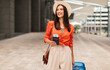 © Prostock-studio - Happy Tourist Lady In Hat Holding Passport And Boarding Pass Walking With Luggage At Modern Airport Outdoors, Looking Away, Advertising Travel Offer. Passenger With Suitcase Arriving At Terminal